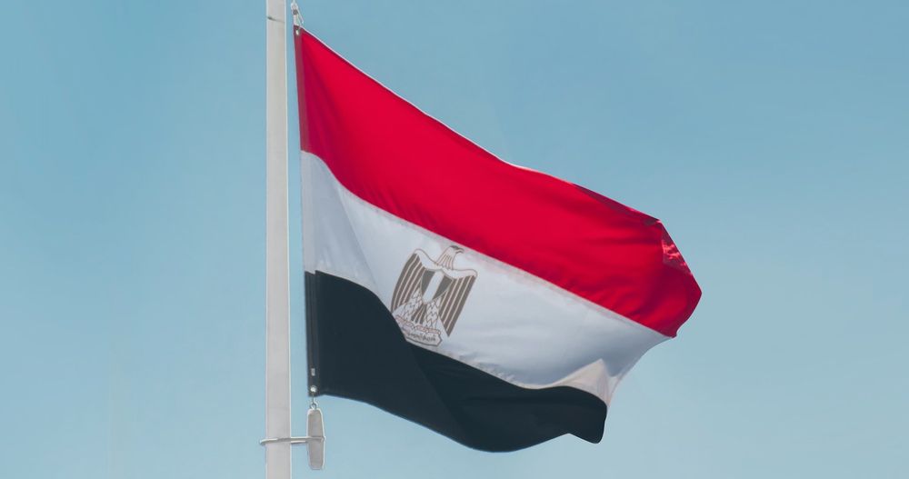 The flag of Egypt flying in the wind against a blue sky background. 