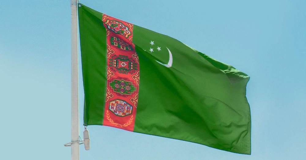The flag of Turkmenistan flying in the wind against a blue sky background. 