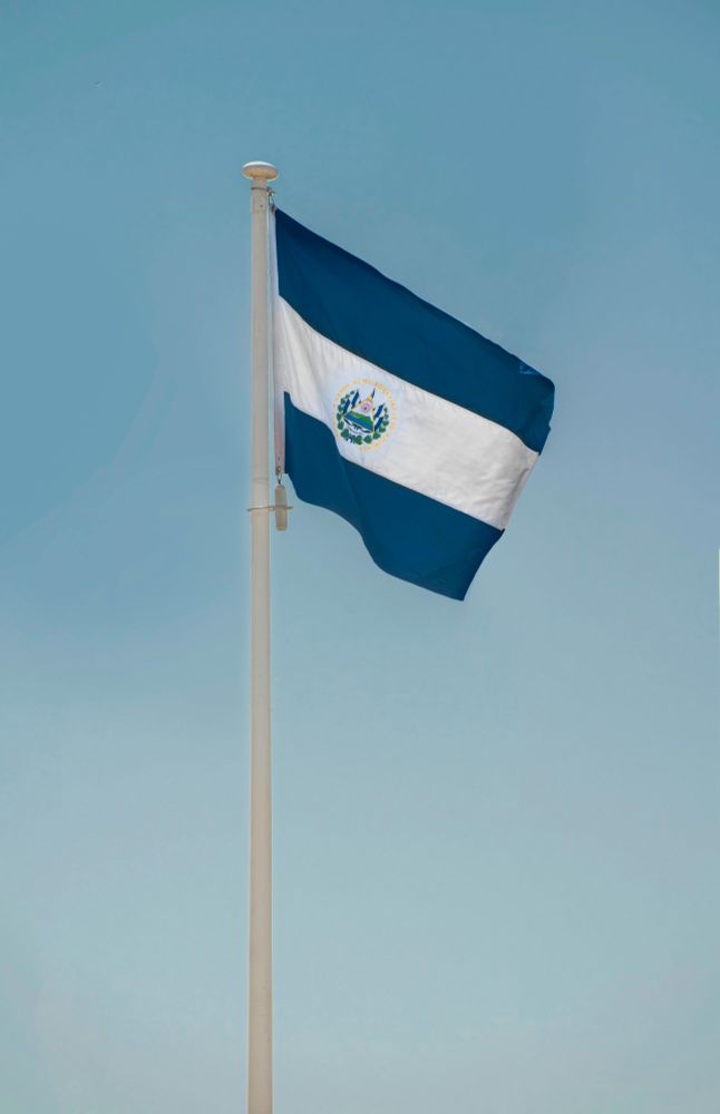 The flag of El Salvador, blowing from a pole against a blue sky
