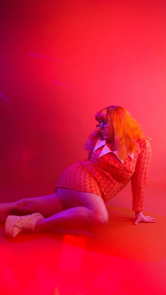 Lady with a big butt wearing short orange dress with long orange hair and glasses