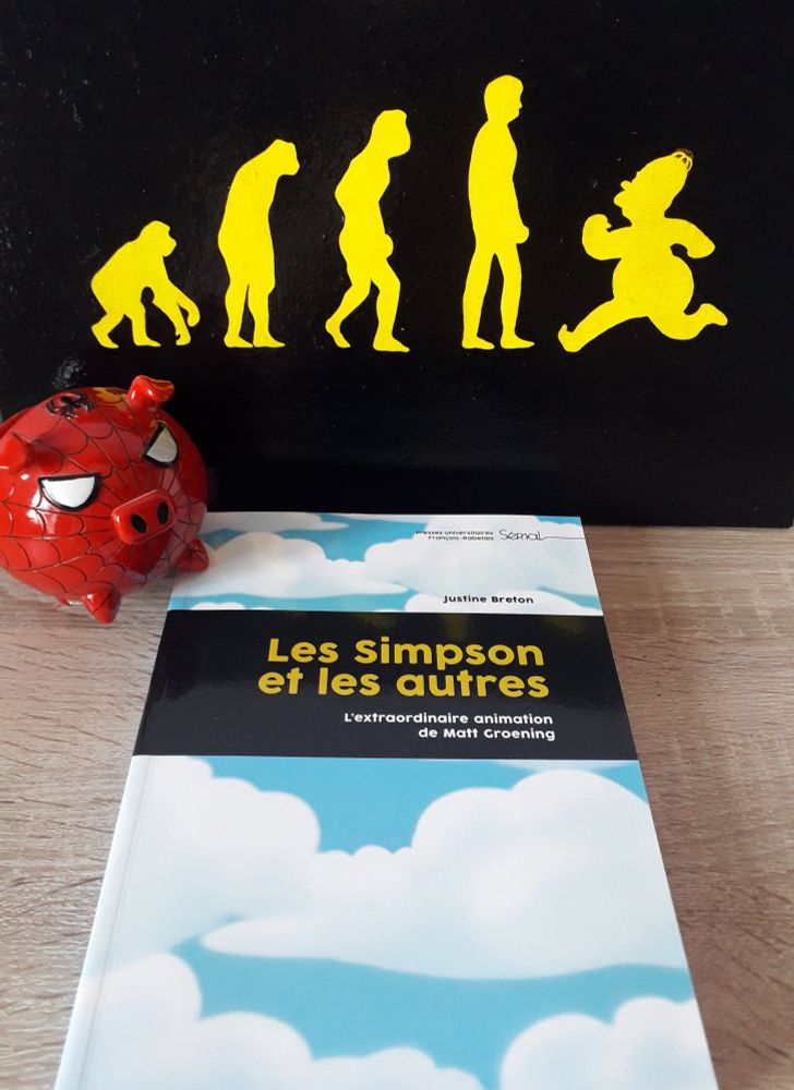 Livre Les Simpson et les autres, avec à gauche une figurine de Spider Cochon (un cochon aux couleurs de Spider-Man, rouge avec une toile noire) et à l'arrière-plan un dessin de l'évolution de l'être humain, jaune sur fond noir, allant de gauche à droite d'un singe à Homer Simpson, lequel fait demi-tour et semble remonter le cours de l'évolution.