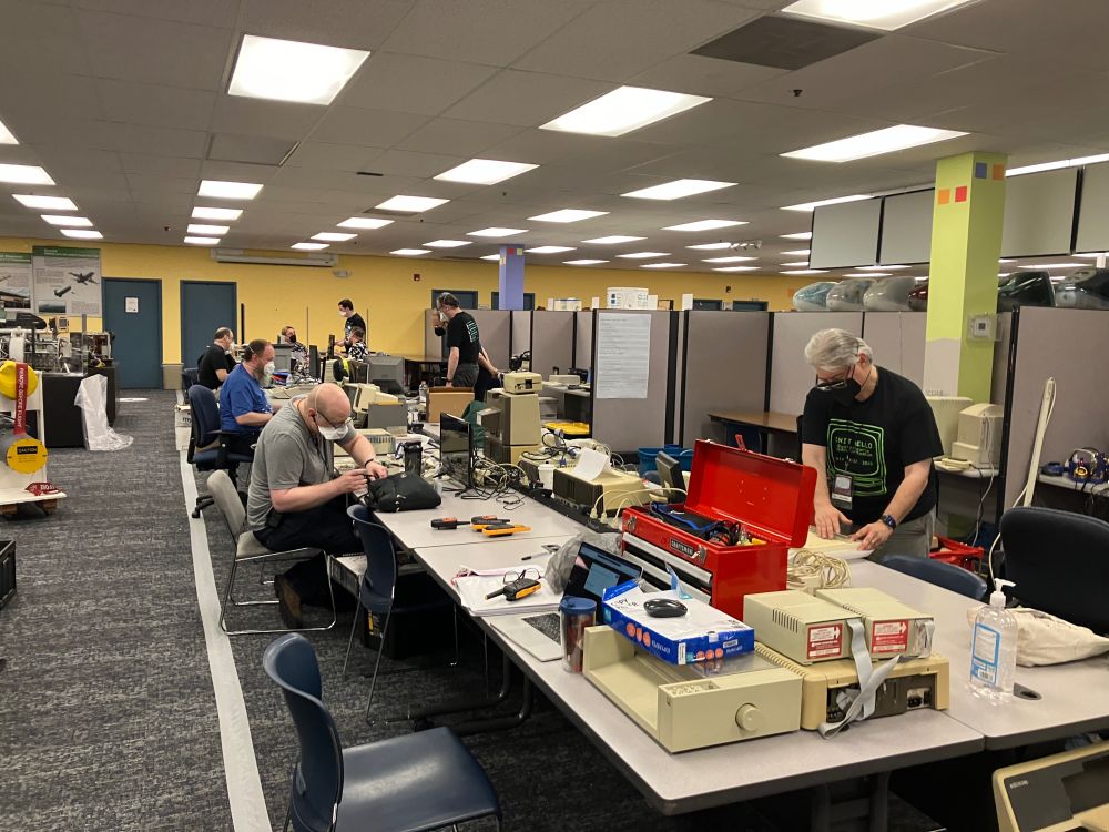 Various folks at tables with retro computers 