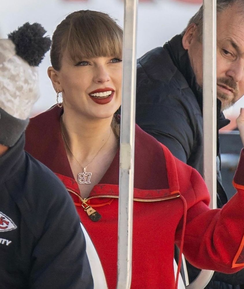 taylor smiling, she’s wearing a red zip up hoodie