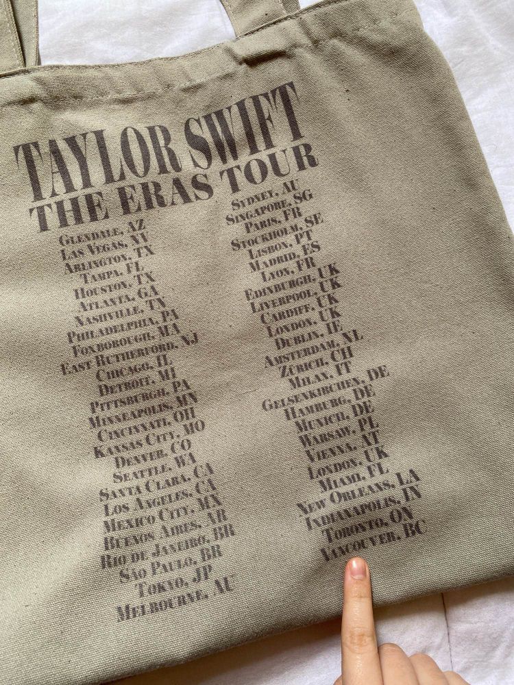 the back of the tote bag shows the cities that taylor swift toured in, and i pointed my finger to the last city (vancouver)