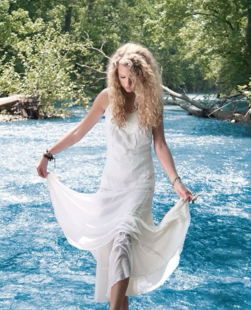 taylor swift in a white dress, in a lake/river with trees in the background