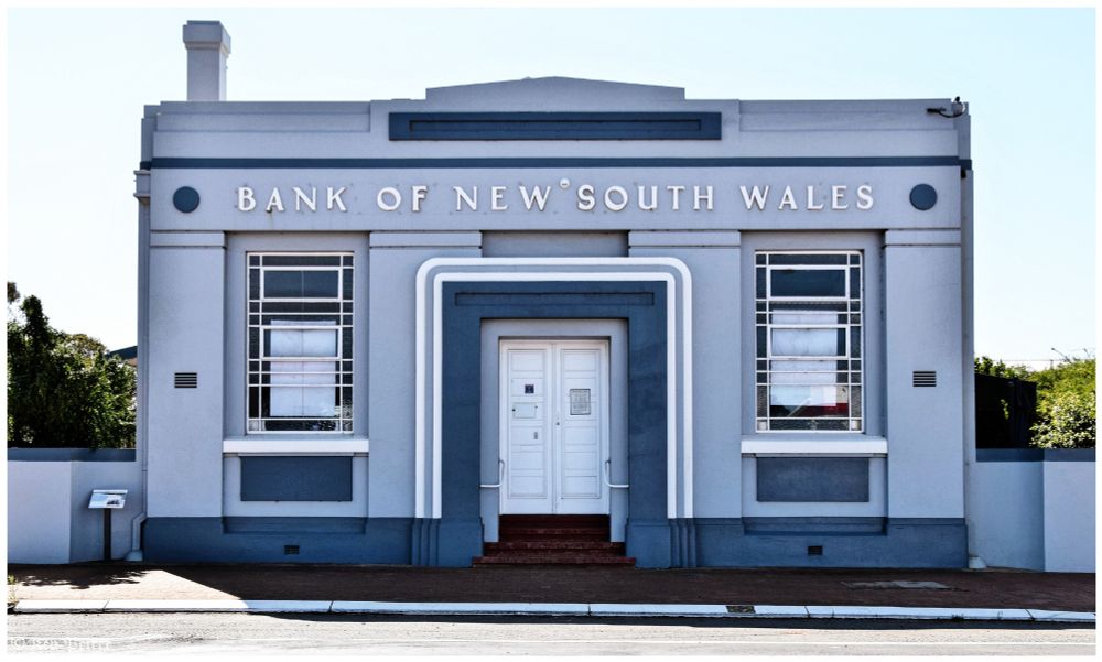 Front view of the historic Bank of New South Wales building, featuring a symmetrical facade with two large arched windows flanking a central entrance.

The building is painted in muted blue-gray tones, with white geometric detailing framing the doorway. "Bank of New South Wales" is displayed prominently above in clean serif lettering, evoking a sense of permanence and tradition.

The design blends classical elegance with regional charm.