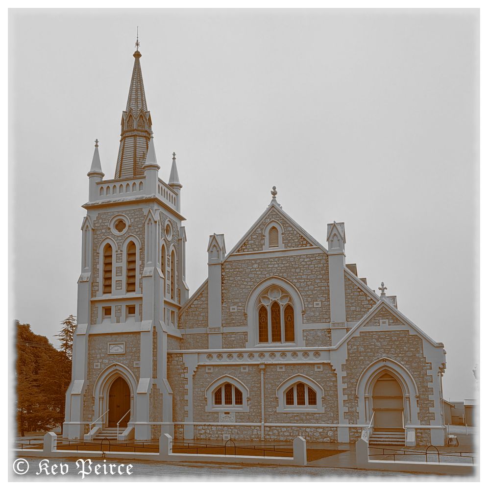 Gothic-style church with a tall steeple, stone facade, white accents, and stained glass windows.

The building features pointed arches, decorative trim, buttresses, and two main entrances with steps. A cross tops the spired steeple.

Image credit: Kev Peirce.