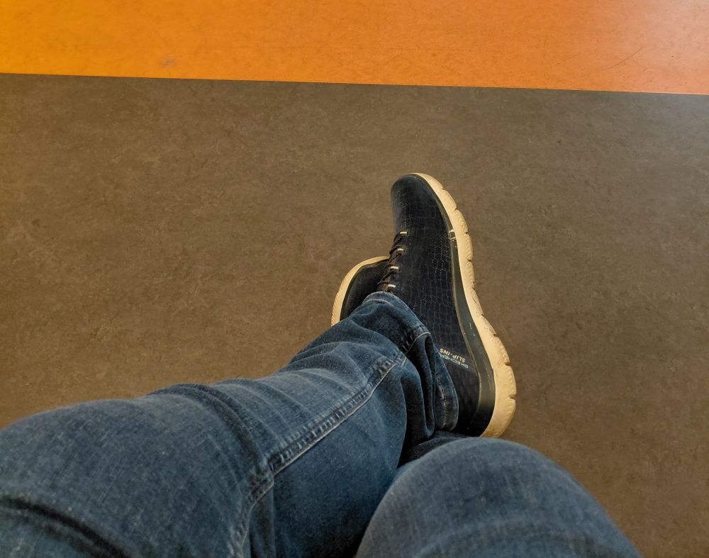 Füße in blauen Sneakers auf orange- grünem Linoleum