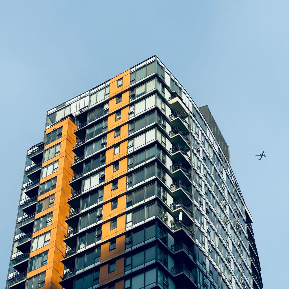 An apartment building with a plane in the sky behind it
