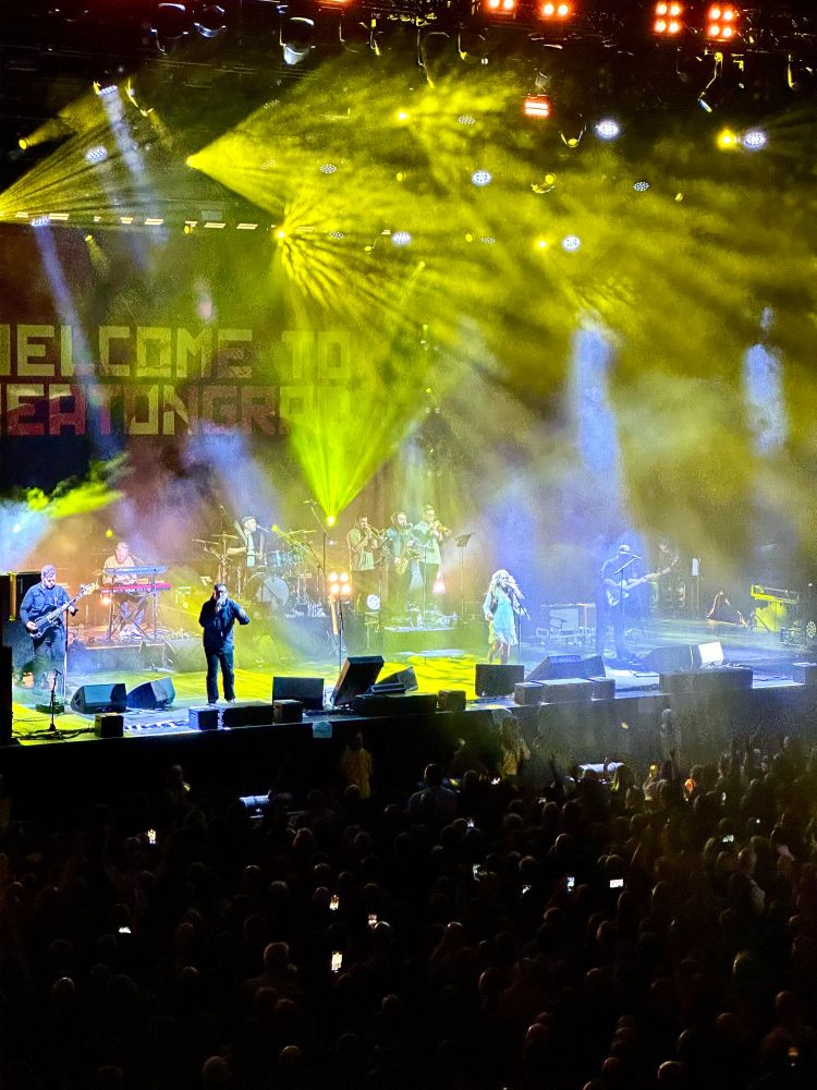 Paul Heaton & Rianne Downey on stage with bright yellow and blue lights.