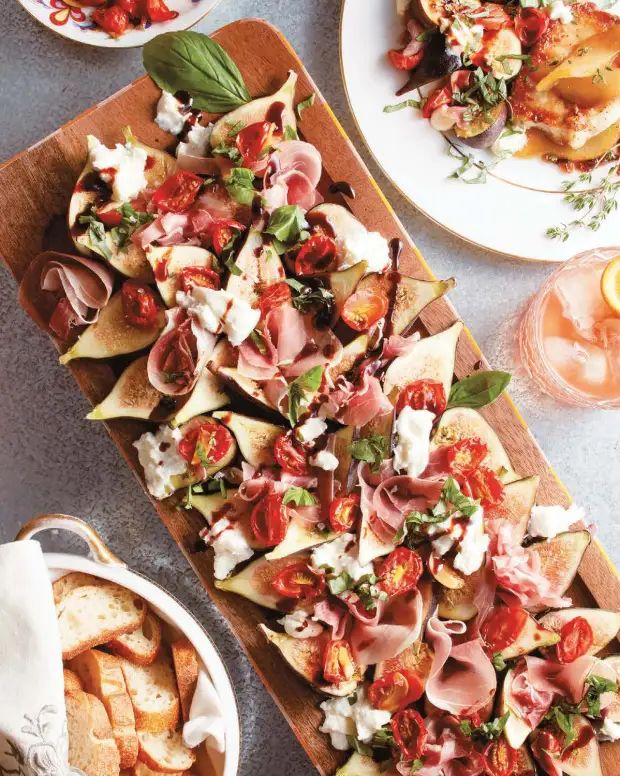 Fig, prosciutto, and burrata salad with roasted tomatoes, fresh basil, and balsamic glaze, arranged on a serving platter.