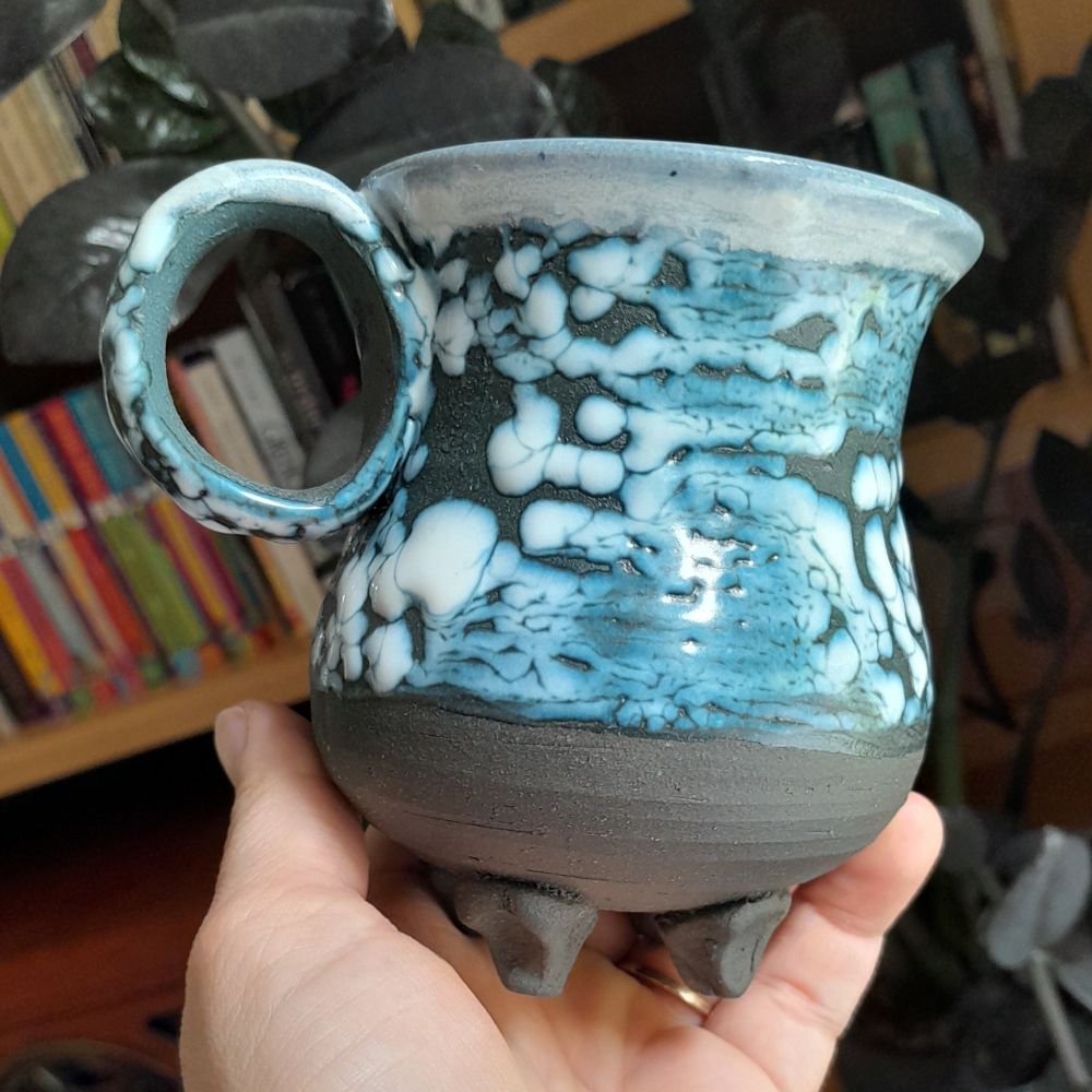A black mug with small feet and white crawl glaze