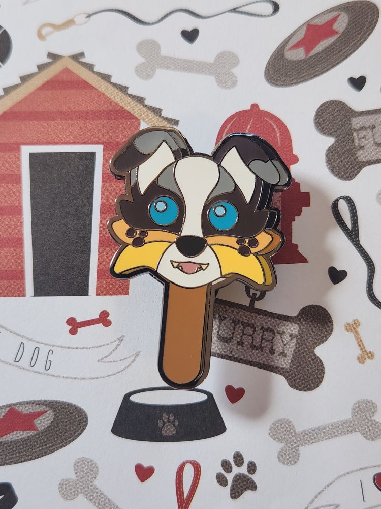 An enamel pin of an Australian Shepherd shaped like a gumball popsicle
