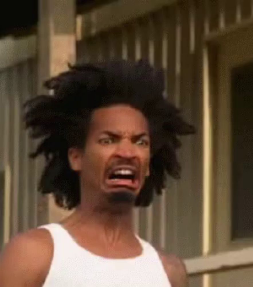 a man with dreadlocks and a beard is making a funny face while wearing a white tank top .