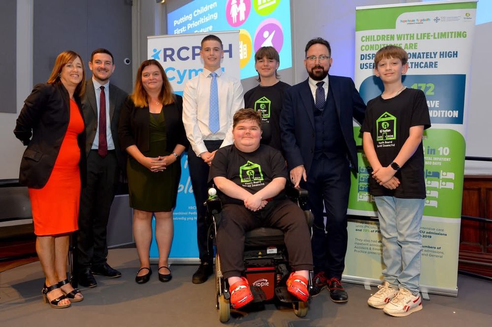 Sioned Williams MS standing on a stage with three other MSs in the Senedd Pierhead building with young people who are representatives and Chair of Tŷ Hafan Children's Hospice youth board.
