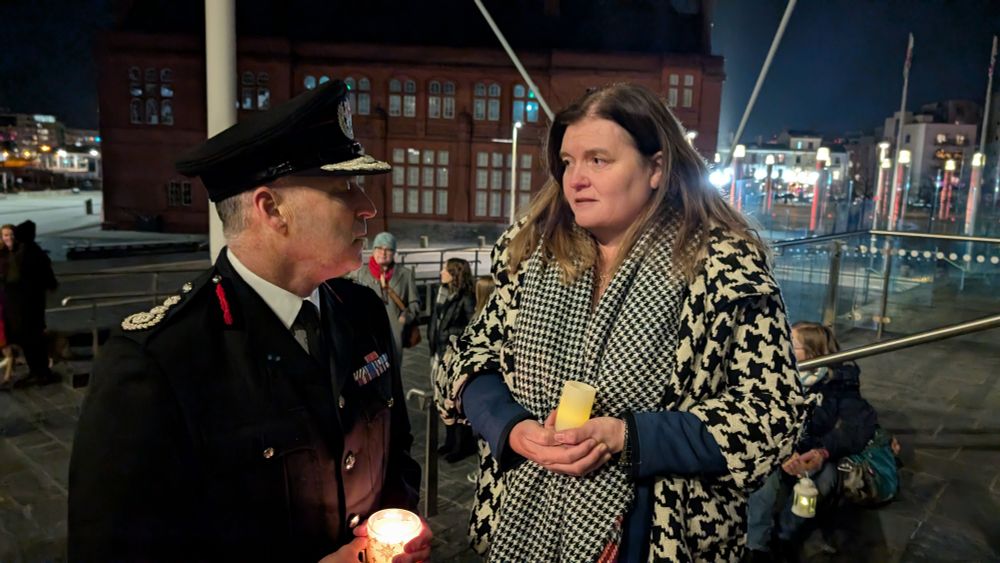 Sioned Williams is talking to a man in uniform. They are both holding candles.