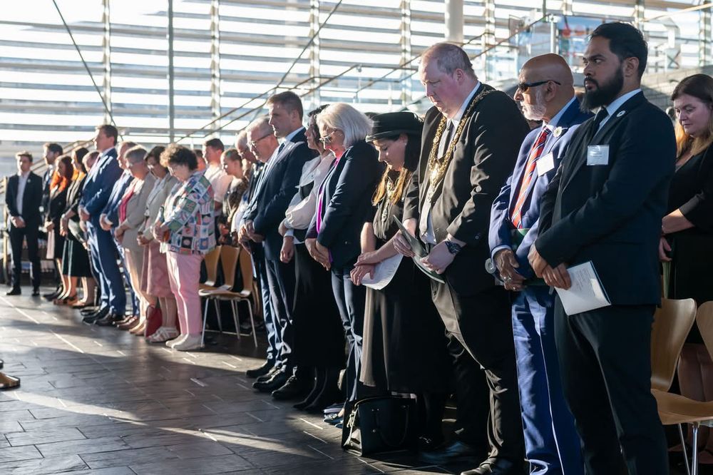 Attendees standing with bowed heads at the memorial event at the Senedd.