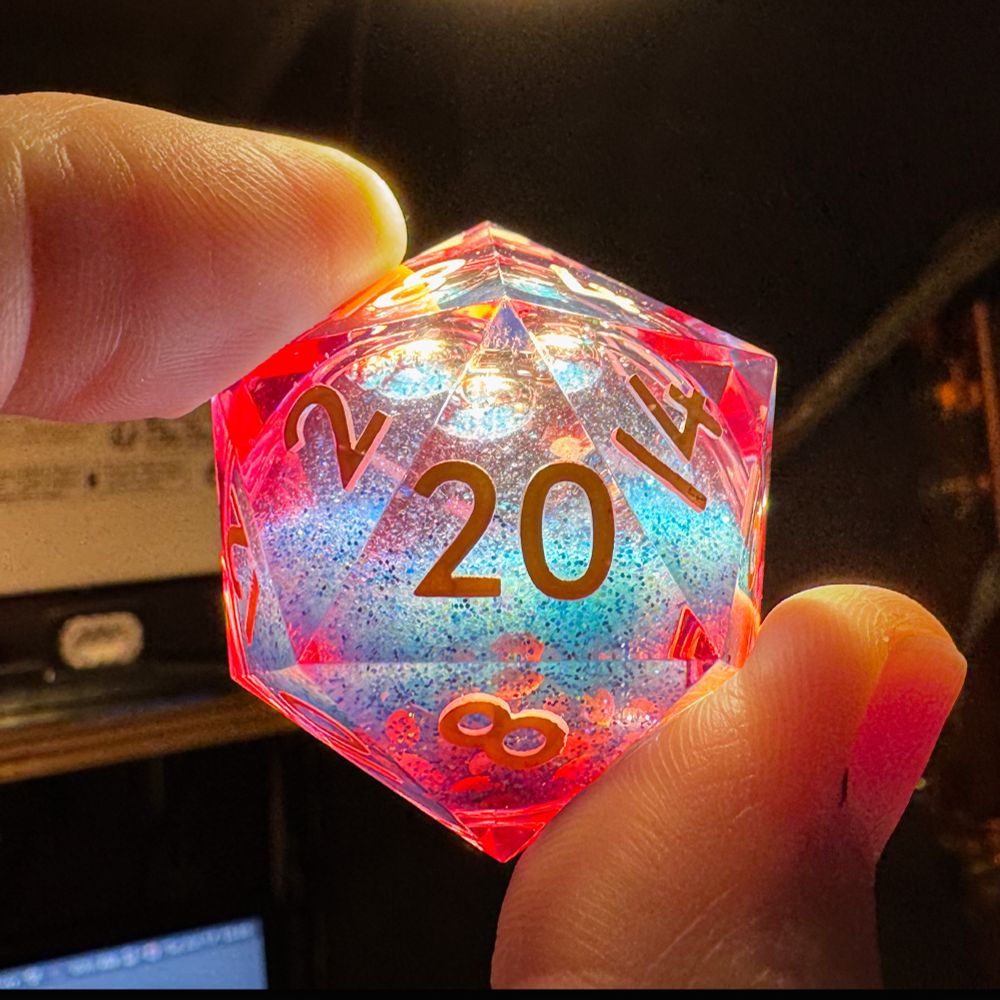 a d20 die being held up to the light revealing pink tinged vertices and a blue sparkly central core filled with liquid.