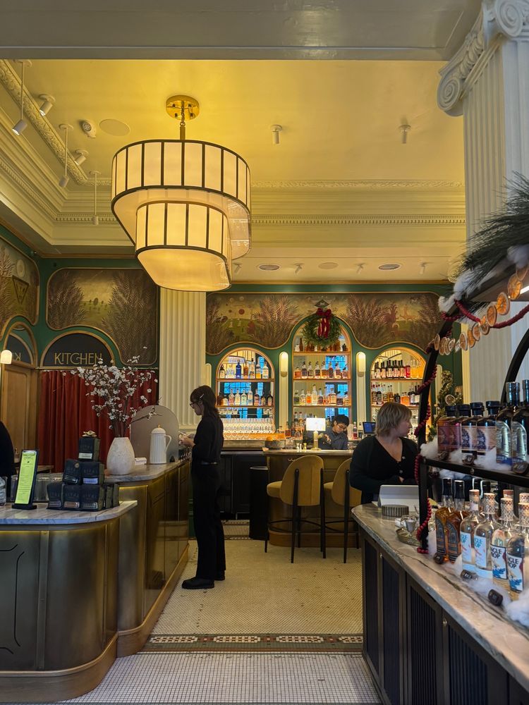 Festive botanical murals at tops of deep green walls in fanciful dining space, coffee counter, and bar in trendy Rittenhouse spot. Mosaic tile floor below has vintage vibes 