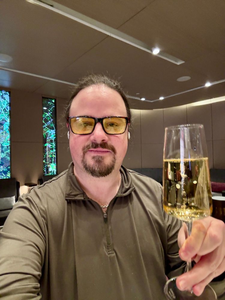 man with goatee wearing glasses looks at camera holding glass of champagne 