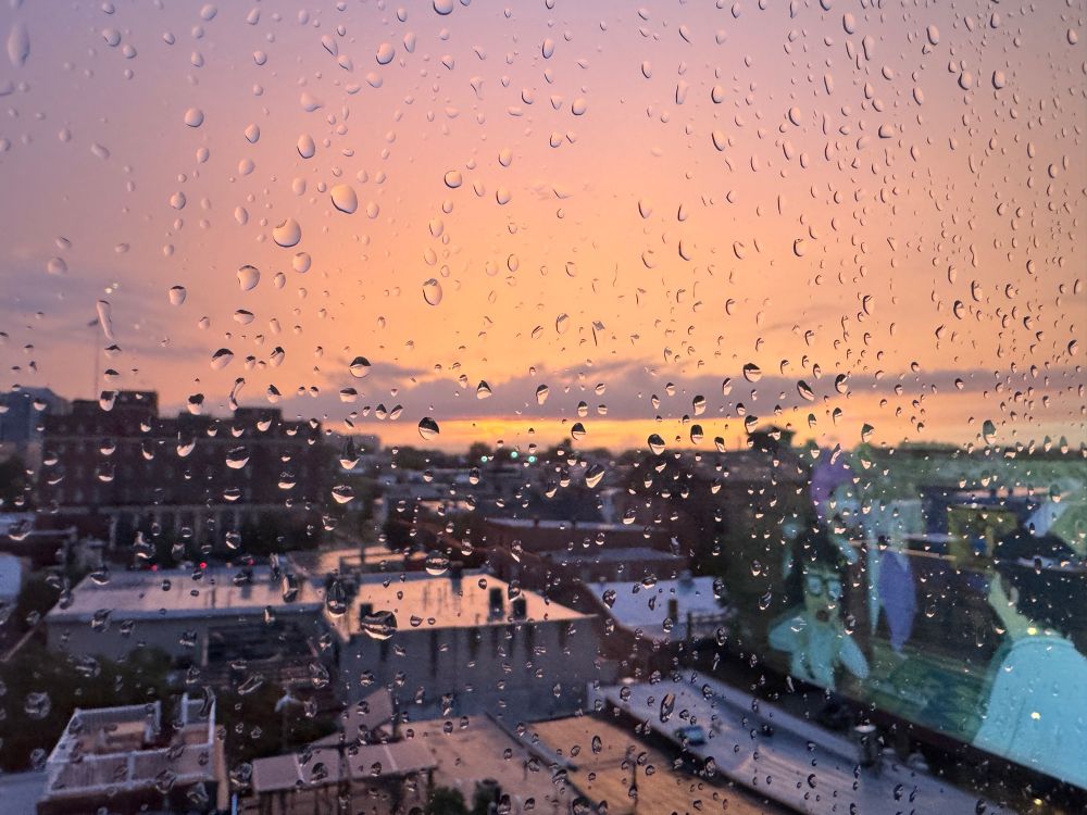 glowing orange sky seen throw a window sprinkled with raindrops at sunset in Philly 