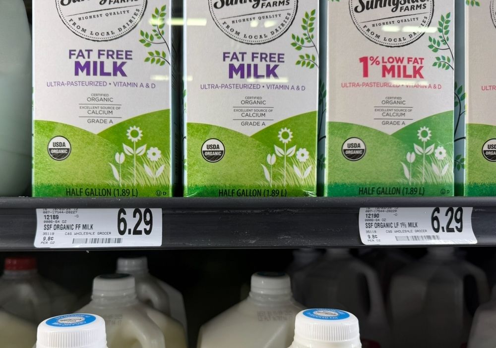 A refrigerated dairy section in a U.S. grocery store showing milk cartons on a shelf that cost $6.29 for half a gallon (or 1.88 liters).