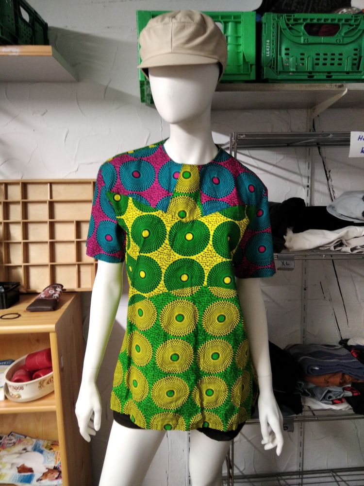 Farbenprächtige gekleidete Schaufensterpuppe mit Mütze. Im Hintergrund Regale mit allerlei.