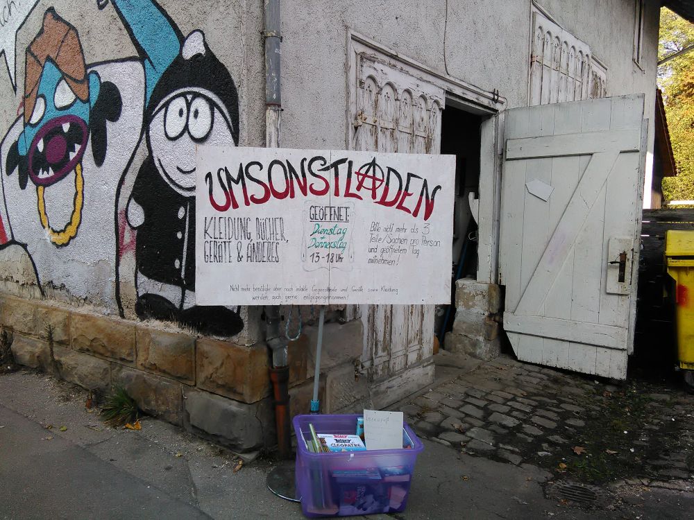 Ladenschild des Umsonstladens vor dem offenen Scheunentor.