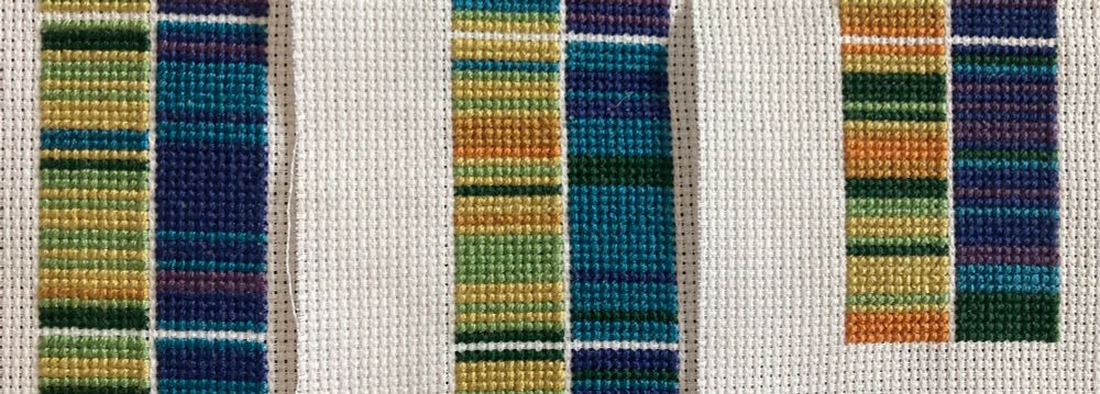 Three pieces of cross stitch with stripes in a rainbow of colours, depicting temperature highs and lows in May 2023, 2024 and 2025