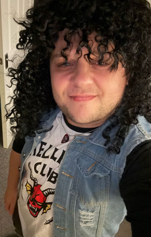 It’s Matteh, dressed as Eddie Munson from stranger things, in a dark curly wig, hellfire club shirt and denim cutoff. 