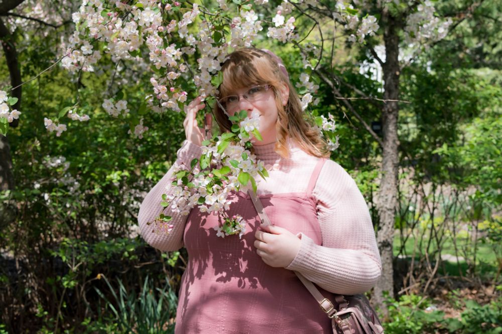 Blonde wide girl wearing all pink poses among the apple blossoms