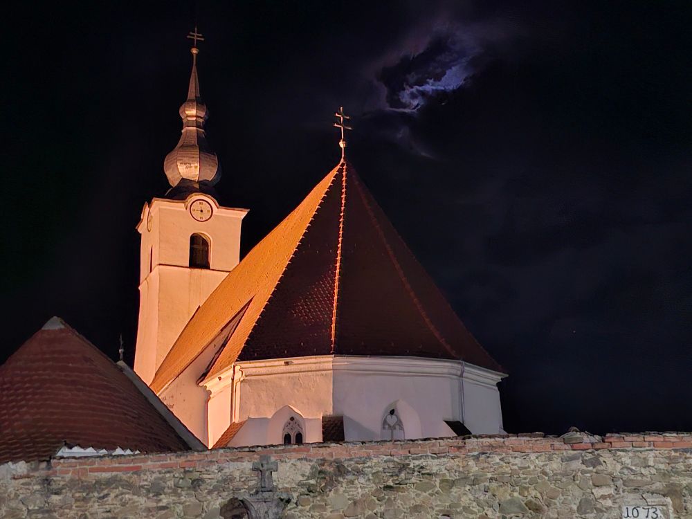 Picture of a church at night with cloud covered moon behind 