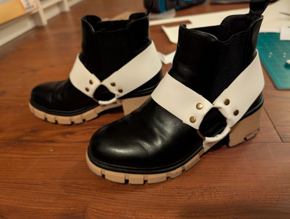 Black Chelsea boots with three white boot straps connected by two O-rings and rivets.