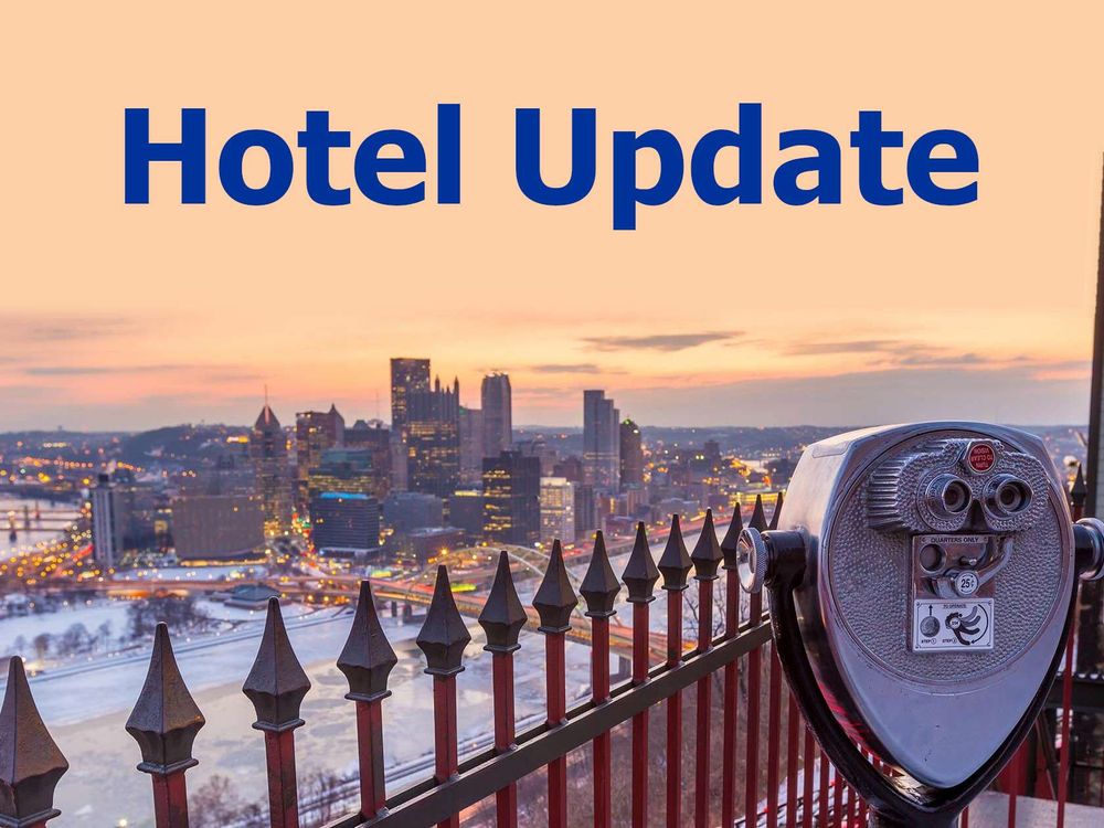 A photograph of downtown Pittsburgh as seen from an observation deck on the south bank of the Monongahela River, near the Duquesne Incline. In the foreground is a red and brown wrought iron fence and a coin-operated set of binoculars. In the midground is the Monongahela River (partially covered in snow and ice) and the Fort Pitt Bridge. To the left of the background is Point State Park and the host hotel (Wyndham Grand), and to the right in the background is the rest of downtown Pittsburgh. At the top of the image are the words 'Hotel Update'.