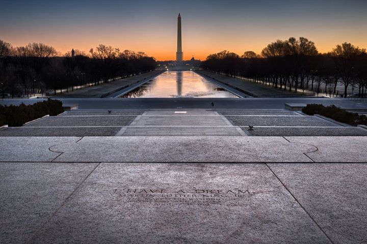 A photograph taken from the steps of the Lincoln Memorial in Washington, DC. In the foreground is the inscription denoting the spot from which Dr. King delivered his 'I Have a Dream' speech. The photograph looks outward down the length of the reflecting pool. The Washington Monument is in the background.