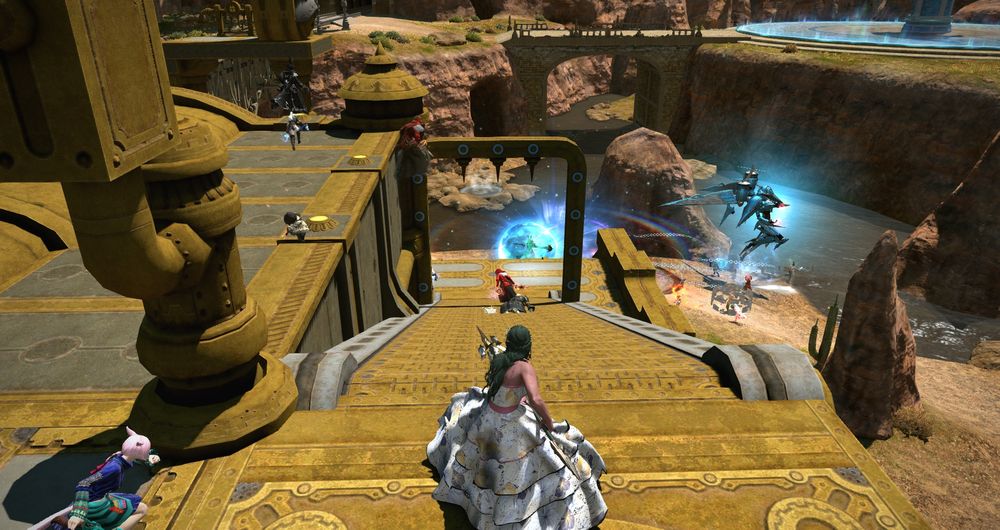 The Rival Wings platform in the middle of the map is shown from the top of the stairs. A woman with dark green hair, in a flowing multi-layered white floral dress, is shown in 3rd person. She's holding a spear and defending the platform. Ahead of her, there are some people exploding and dying, and a pink-haired teammate is running towards her from the left.