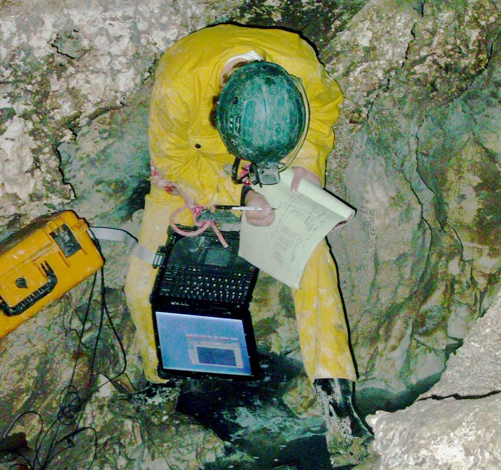 Karst scientist in a cave taking notes on instrument readings near an underground stream.