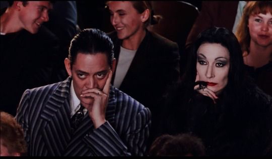 Gomez and Morticia Addams looking bored while sitting in a theater among normal people.