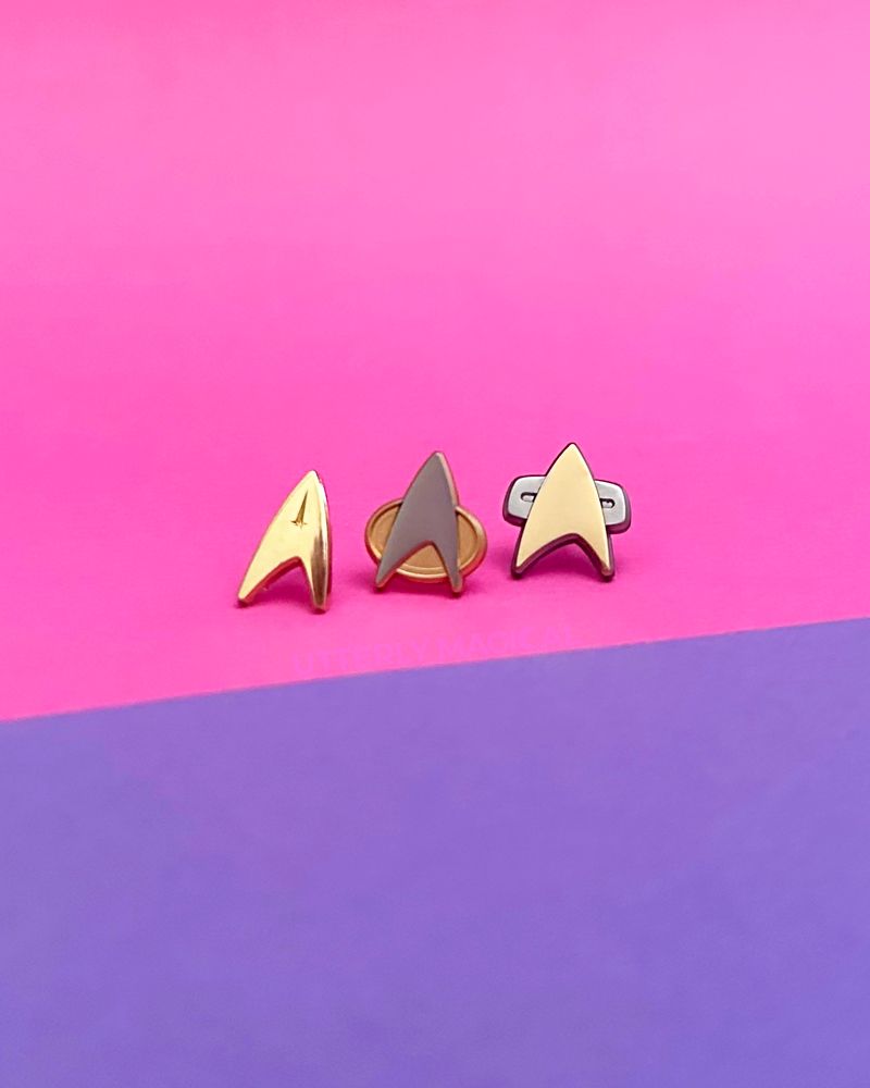 Three mini enamel pins on a pink and purple background. 