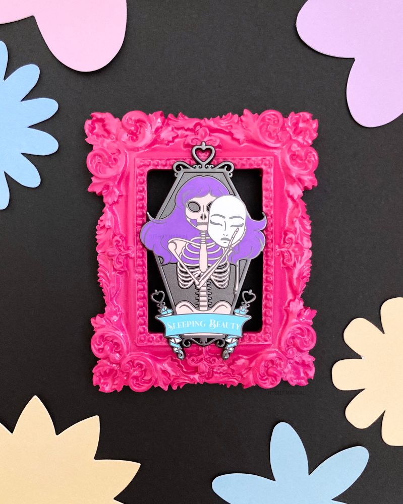 An enamel pin on a pink frame on a black background with colorful flowers all around. 
