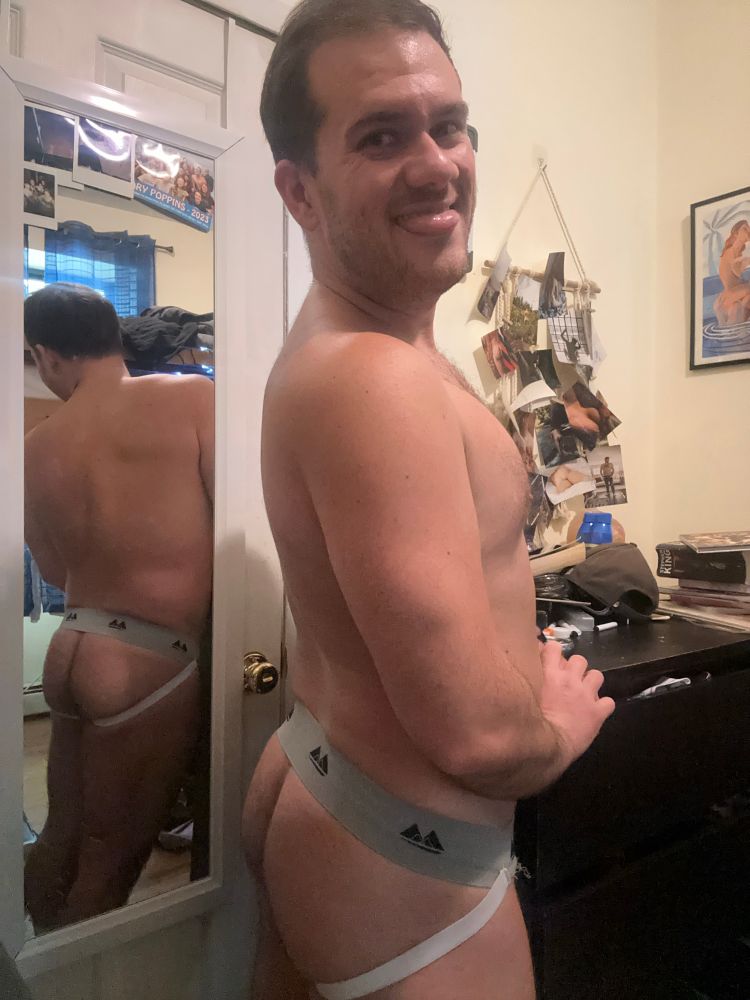White male in a messy room posing in a jockstrap by his mirror 