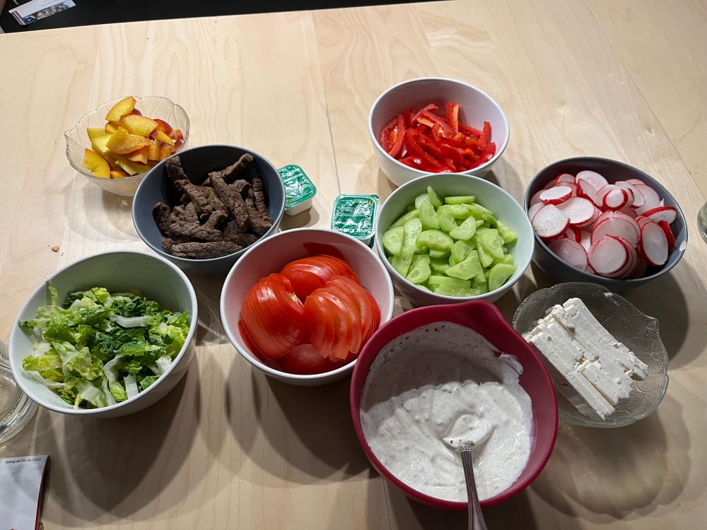 Einzelteile für Wraps. Ohne Wraps. Von links nach rechts: Feingeschnittener Salat, Pfirsich, Steakstreifeb, Tomate, Sour Creme vom goldenen M, selbst gemachte Joghurtsauce, Gurke, Paprika, Feta und Radieschen 