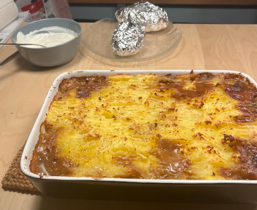Fertiger Cottage Pie auf dem Esstisch. Im Hintergrund sieht man das Alternativ Essen für das Vegetarische Kind: Backkartoffeln mit Joghurt 