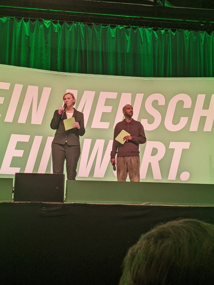 Auf der Bühne stehe Nina Stahr und Philmon Ghirnai und begrüßen das Publikum.