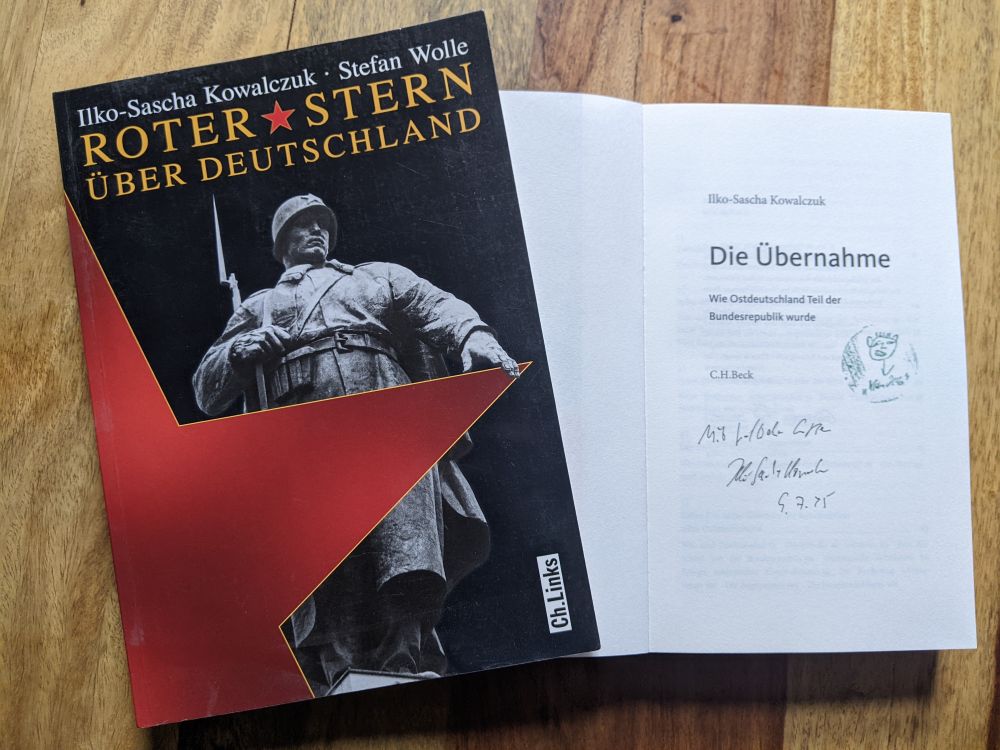 Zwei Bücher von Ilko-Sascha Kowalczuk liegen auf einem Tisch. Titel: Roter Stern über Deutschland und Die Übernahme. Das zweite Buch ist aufgeschlagen und zeigt eine kurze Widmung des Autors. Zitat: "Mit lieben Grüßen Ilko-Sascha Kowalczuk"
