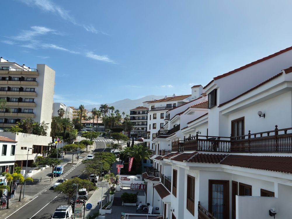 Sunny view from a balcony looking over a busy street with a mountain in the background.