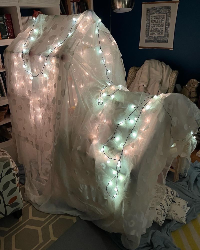 A taller fort built around a Pikler triangle and decorated with Christmas lights. 