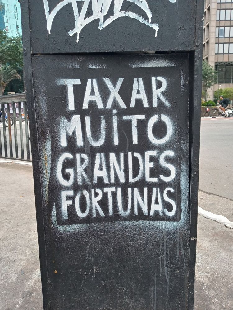 Stencil com a mensagem "Taxar muito grandes fortunas" em área urbana
