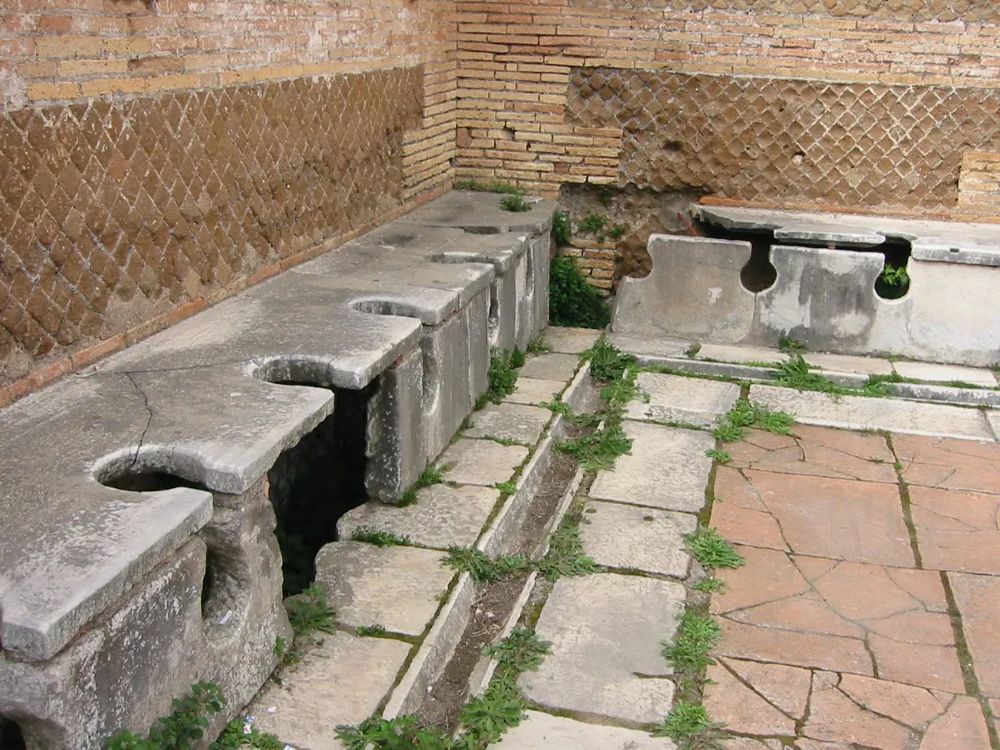 photo of public roman toilets that shows the gutter running in front of the toilets