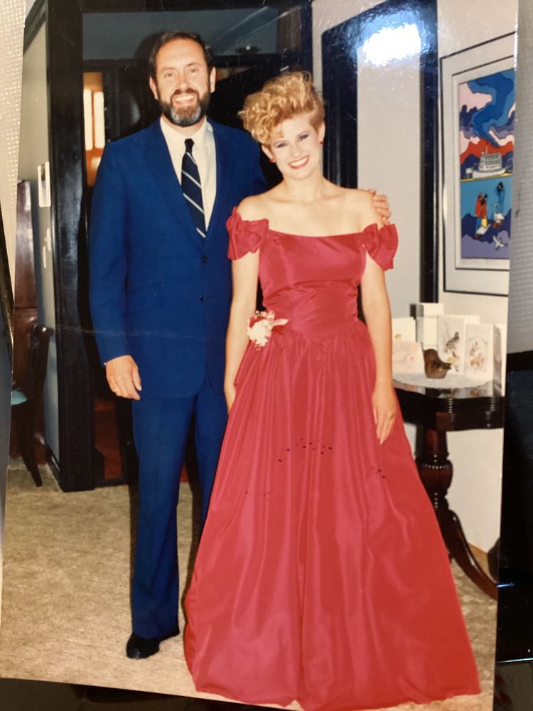 The author, in a red prom dress with a corsage at the waist, poses with her father, wearing a blue suit and striped tie. 